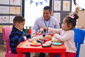 Hispanic man with boy and girl playing supermarket game sitting on table at kindergarten