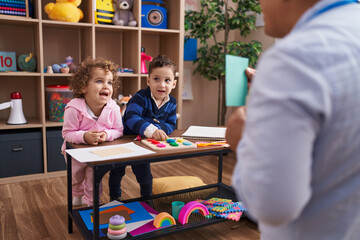 Hispanic man with boy and girl playing with vocabulary game standing at kindergarten
