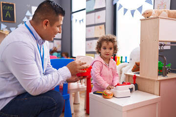 Fototapeta premium Hispanic man and girl playing supermarket game sitting on table at kindergarten