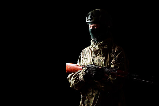 An armed soldier in military uniform holds a rifle in his hands on a black background, studio