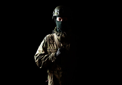 An armed soldier in military uniform holds a rifle in his hands on a black background, studio
