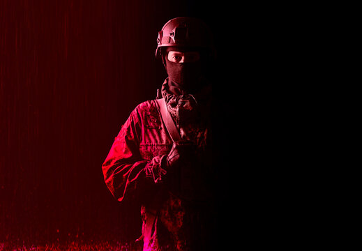 An armed soldier in military uniform holds a rifle in his hands on a black and red background, studio