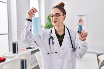 Young hispanic girl holding medical asthma inhaler at the clinic winking looking at the camera with...