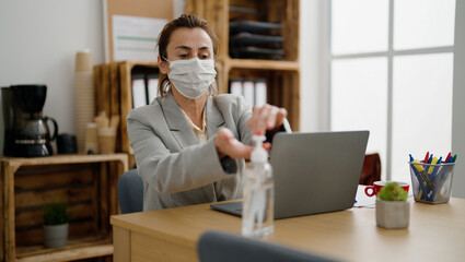 Middle age hispanic woman business worker wearing medical mask using sanitizer gel hands at office - obrazy, fototapety, plakaty