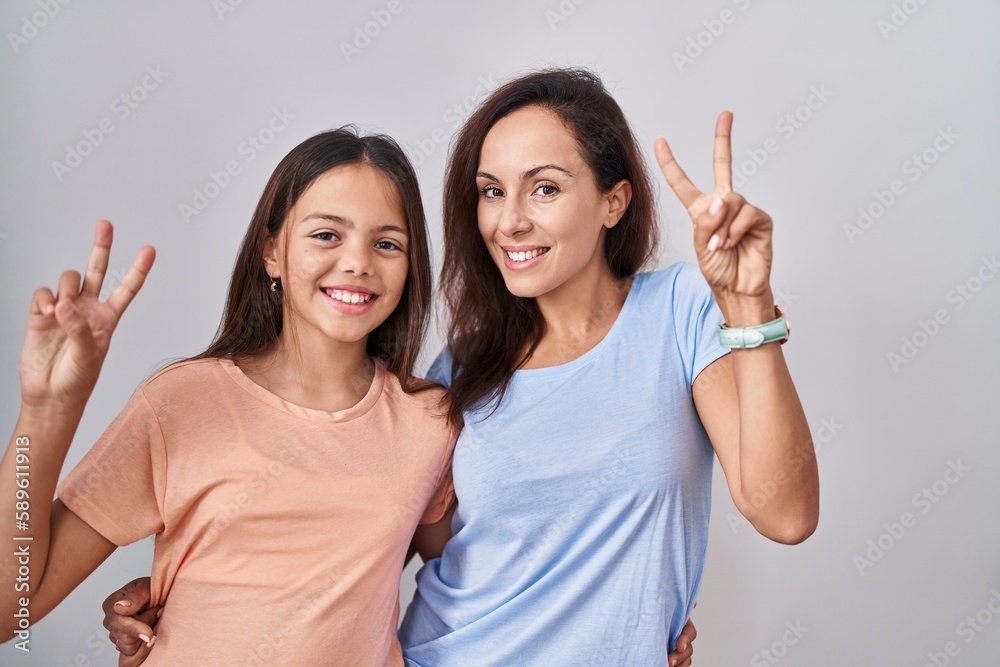 Canvas Prints Young mother and daughter standing over white background smiling looking to the camera showing fingers doing victory sign. number two.