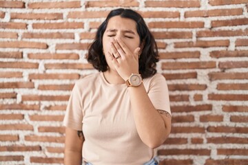 Young hispanic woman standing over bricks wall bored yawning tired covering mouth with hand. restless and sleepiness.