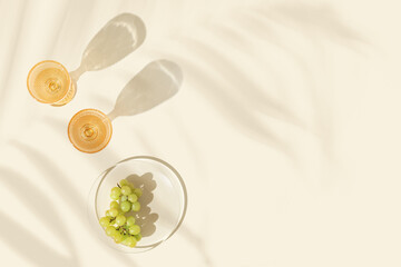 Wine glasses with white wine and green grape on beige background palm leaf shadow at sunlight. Summer alcohol drinks concept, colored glassware. Top view minimal aesthetic still life photo