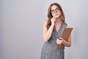 Caucasian woman wearing glasses and business clothes with hand on chin thinking about question, pensive expression. smiling with thoughtful face. doubt concept.