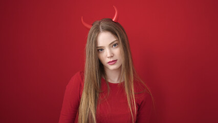 Young blonde woman wearing devil costume with relaxed expression over isolated red background