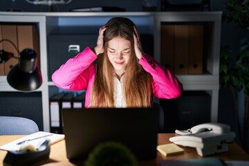 Young caucasian woman working at the office at night suffering from headache desperate and stressed because pain and migraine. hands on head.