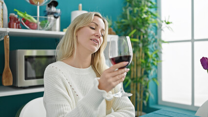 Young blonde woman drinking glass of wine sitting on table at dinning room