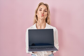 Young caucasian woman holding laptop showing screen looking at the camera blowing a kiss being lovely and sexy. love expression.