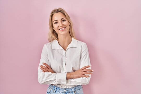 Young caucasian woman wearing casual white shirt over pink background happy face smiling with crossed arms looking at the camera. positive person.