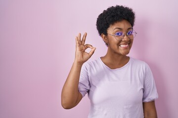 Fototapeta na wymiar Young african american woman standing over pink background smiling positive doing ok sign with hand and fingers. successful expression.