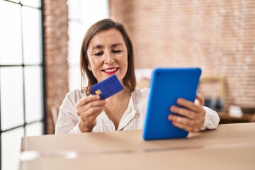 Fototapeta premium Middle age woman using touchpad and credit card standing at new home