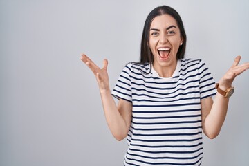 Young brunette woman wearing striped t shirt celebrating crazy and amazed for success with arms raised and open eyes screaming excited. winner concept