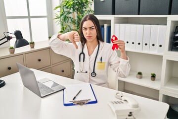 Hispanic doctor woman holding support red ribbon with angry face, negative sign showing dislike with thumbs down, rejection concept