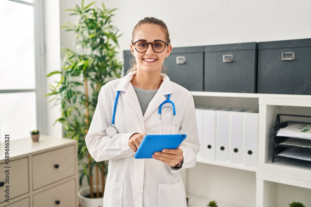 Sticker young blonde woman wearing doctor uniform using touchpad working at clinic