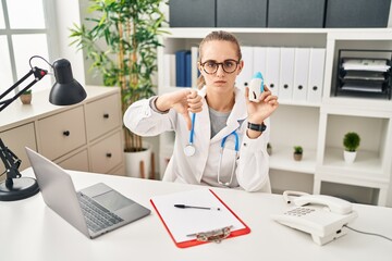 Naklejka na ściany i meble Young doctor woman wearing uniform and stethoscope with angry face, negative sign showing dislike with thumbs down, rejection concept