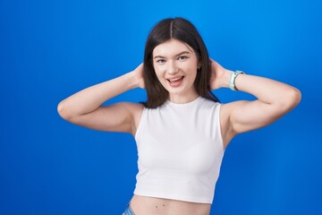 Fototapeta na wymiar Young caucasian woman standing over blue background relaxing and stretching, arms and hands behind head and neck smiling happy