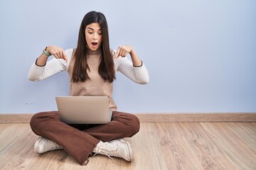 Young brunette woman working using computer laptop sitting on the floor pointing down with fingers showing advertisement, surprised face and open mouth © Krakenimages.com