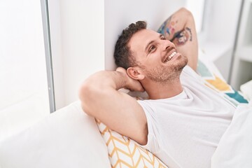 Obraz premium Young hispanic man relaxed with hands on head lying on bed at bedroom