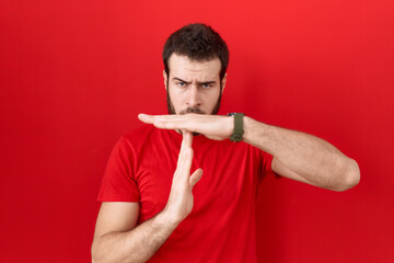Young hispanic man wearing casual red t shirt doing time out gesture with hands, frustrated and...