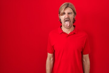 Caucasian man with mustache standing over red background sticking tongue out happy with funny expression. emotion concept.