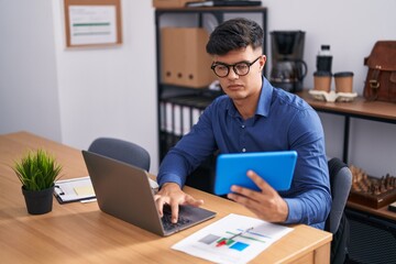 Young hispanic man business worker using touchpad and laptop at office