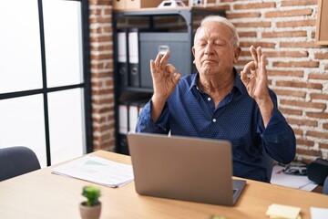 Senior man with grey hair working using computer laptop at the office relax and smiling with eyes closed doing meditation gesture with fingers. yoga concept.