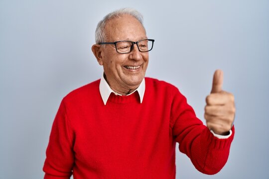 Senior man with grey hair standing over isolated background looking proud, smiling doing thumbs up gesture to the side