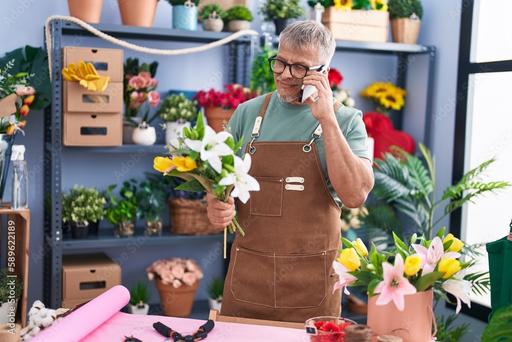 Poster Middle age grey-haired man florist talking on smartphone holding flowers at flower shop