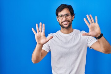 Naklejka premium Handsome latin man standing over blue background showing and pointing up with fingers number ten while smiling confident and happy.