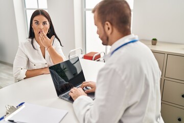 Obraz premium Young hispanic woman at the doctor covering mouth with hand, shocked and afraid for mistake. surprised expression