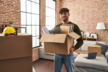 Young arab man smiling confident holding package at new home