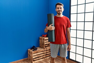 Young hispanic man wearing sportswear holding yoga mat at sport center