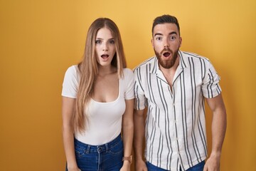 Young couple standing over yellow background afraid and shocked with surprise and amazed expression, fear and excited face.