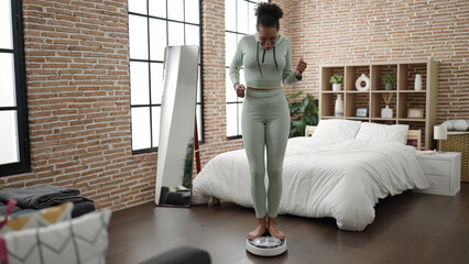 African american woman smiling confident measuring weight using weighing machine at bedroom
