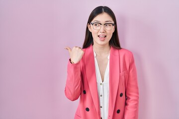 Chinese business young woman wearing glasses smiling with happy face looking and pointing to the side with thumb up.