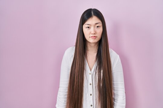 Chinese young woman standing over pink background looking sleepy and tired, exhausted for fatigue and hangover, lazy eyes in the morning.