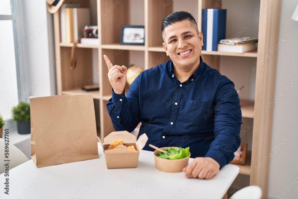 Canvas Prints hispanic young man eating take away food smiling happy pointing with hand and finger to the side