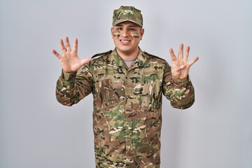 Hispanic young man wearing camouflage army uniform showing and pointing up with fingers number nine while smiling confident and happy.