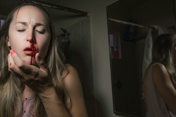 This image shows an injured young woman holding her face with a bloody nose. 