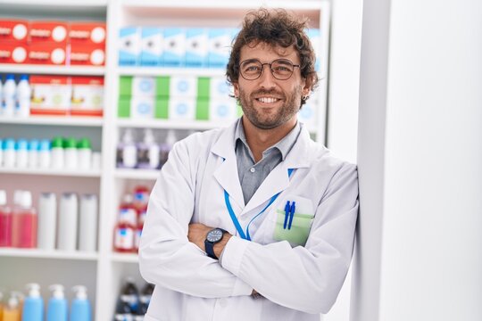 Young hispanic man pharmacist smiling confident standing with arms crossed gesture at pharmacy