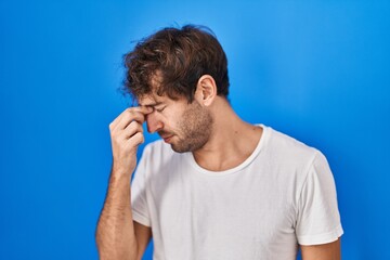 Hispanic young man standing over blue background tired rubbing nose and eyes feeling fatigue and headache. stress and frustration concept.