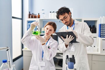 Fototapeta premium Man and woman scientist partners holding test tube writing on clipboard at laboratory