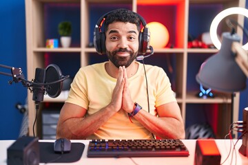 Hispanic man with beard playing video games with headphones praying with hands together asking for...