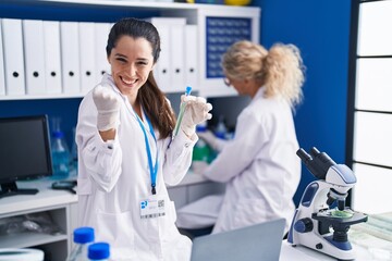 Young hispanic woman working at scientist laboratory screaming proud, celebrating victory and success very excited with raised arms