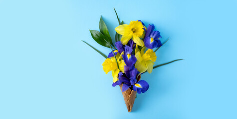 Beautiful composition of yellow and blue flowers in a waffle ice cream cone on a blue background.