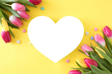 Mother's Day celebration idea. Creative layout made of white heart colorful tulips flowers and small hearts baubles on isolated light yellow background. Flat lay with blank space